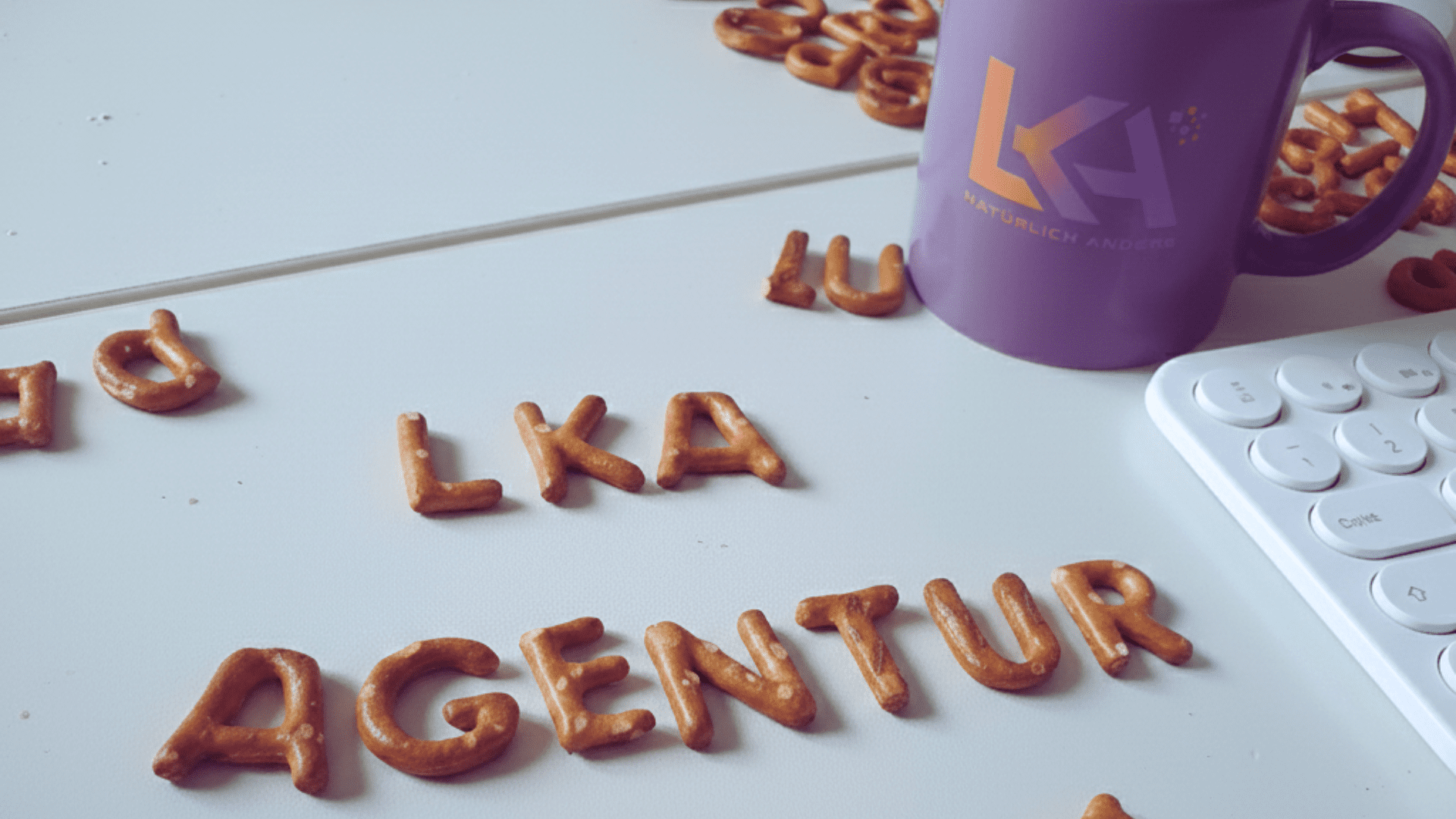 Schreibtisch der LKA-Agentur mit lila Markenbecher, Tastatur und kreativ gelegtem Schriftzug aus Salzgebäck